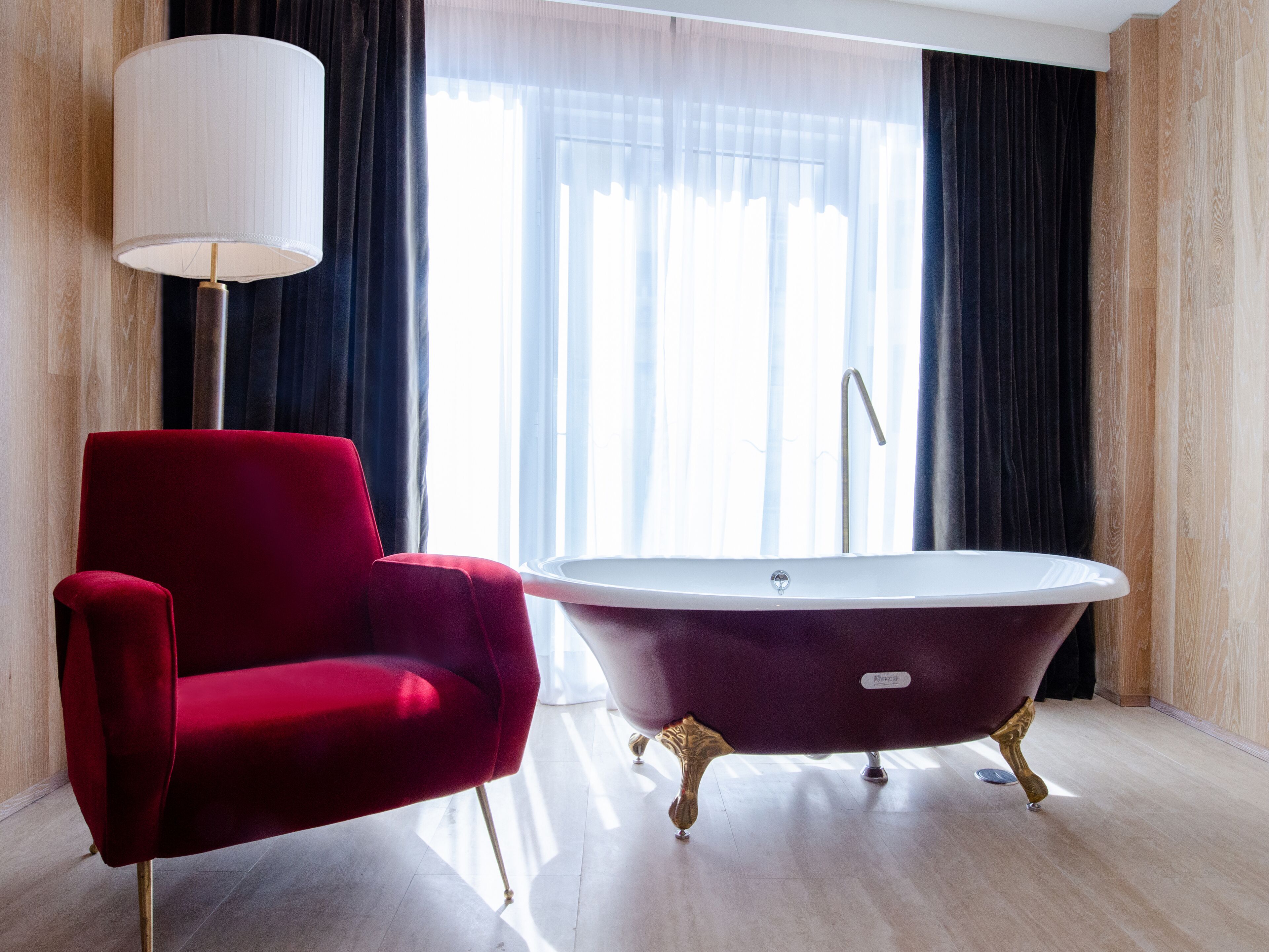 A modern bathroom with a red chair, a freestanding bathtub, and a floor lamp.
