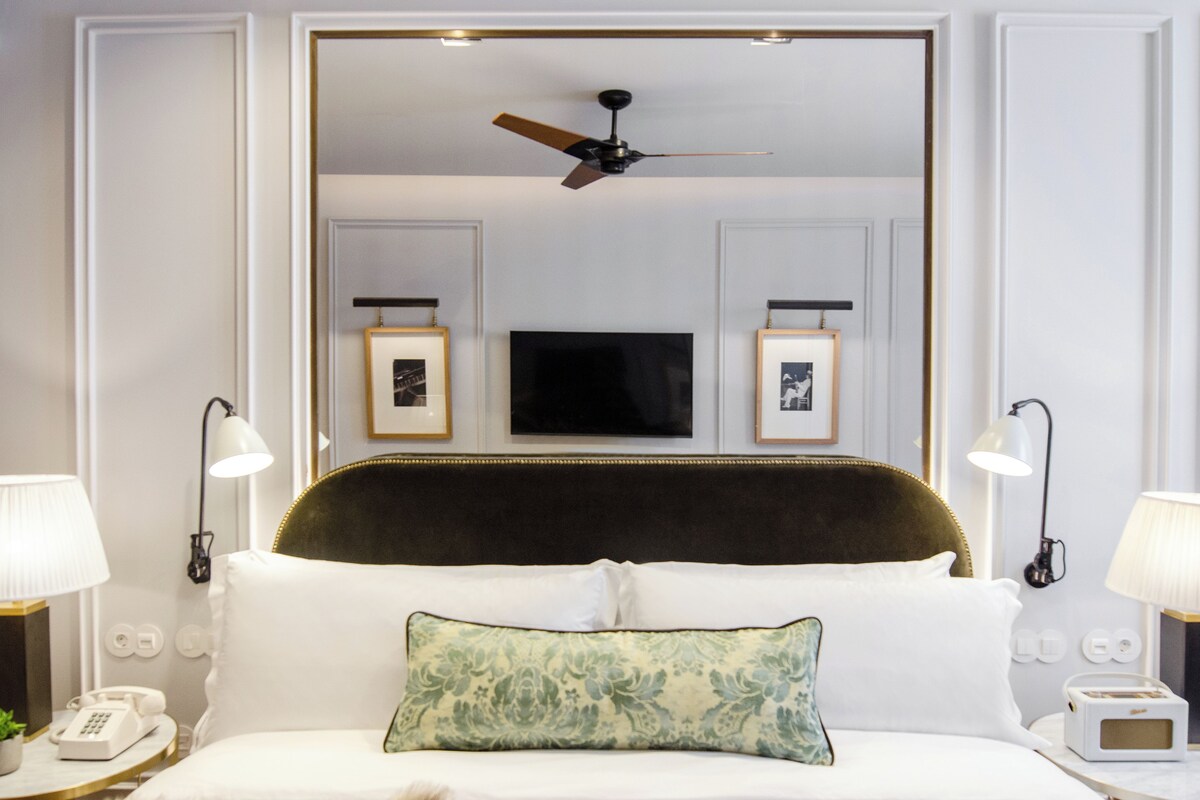 A hotel room with a large bed, a ceiling fan, a TV, and framed pictures on the wall.