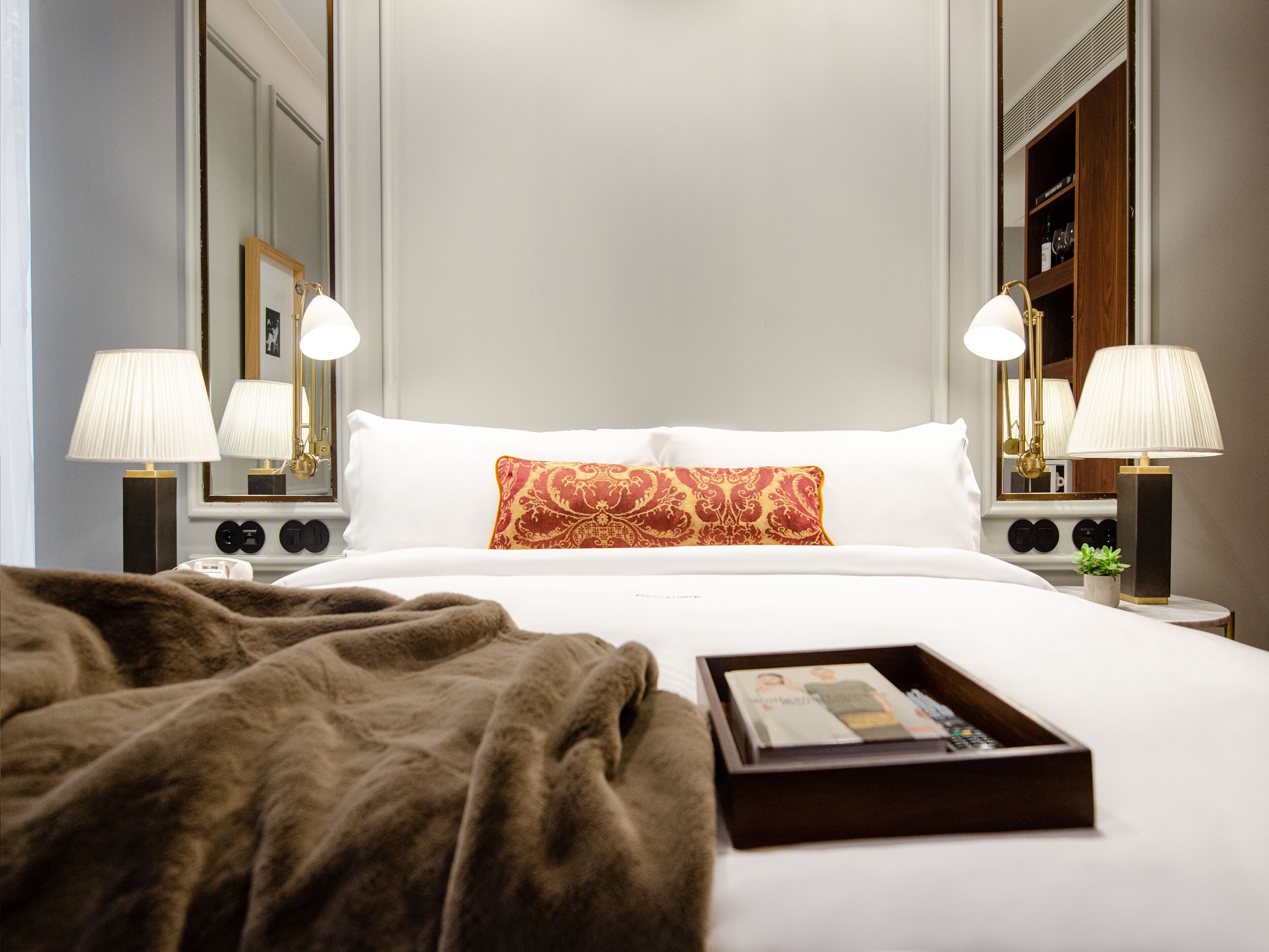 Quarto de hotel com uma cama grande, duas luminárias de cabeceira, uma mesa de cabeceira, um espelho e um armário de madeira.