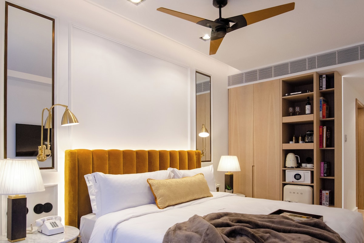 Une chambre d’hôtel comprenant un lit, un ventilateur de plafond, une table de chevet avec une lampe, un téléphone et une bibliothèque.