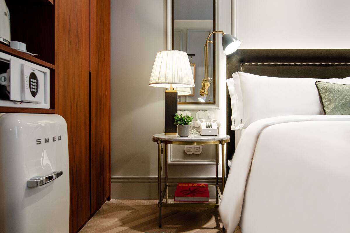 Ein Hotelzimmer mit Bett, Nachttisch, Lampe und einer Minibar.