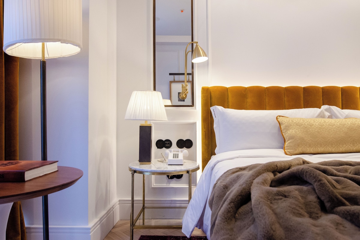 Une chambre d’hôtel avec un lit, une table de chevet, une lampe, un miroir et un livre posé sur une petite table.