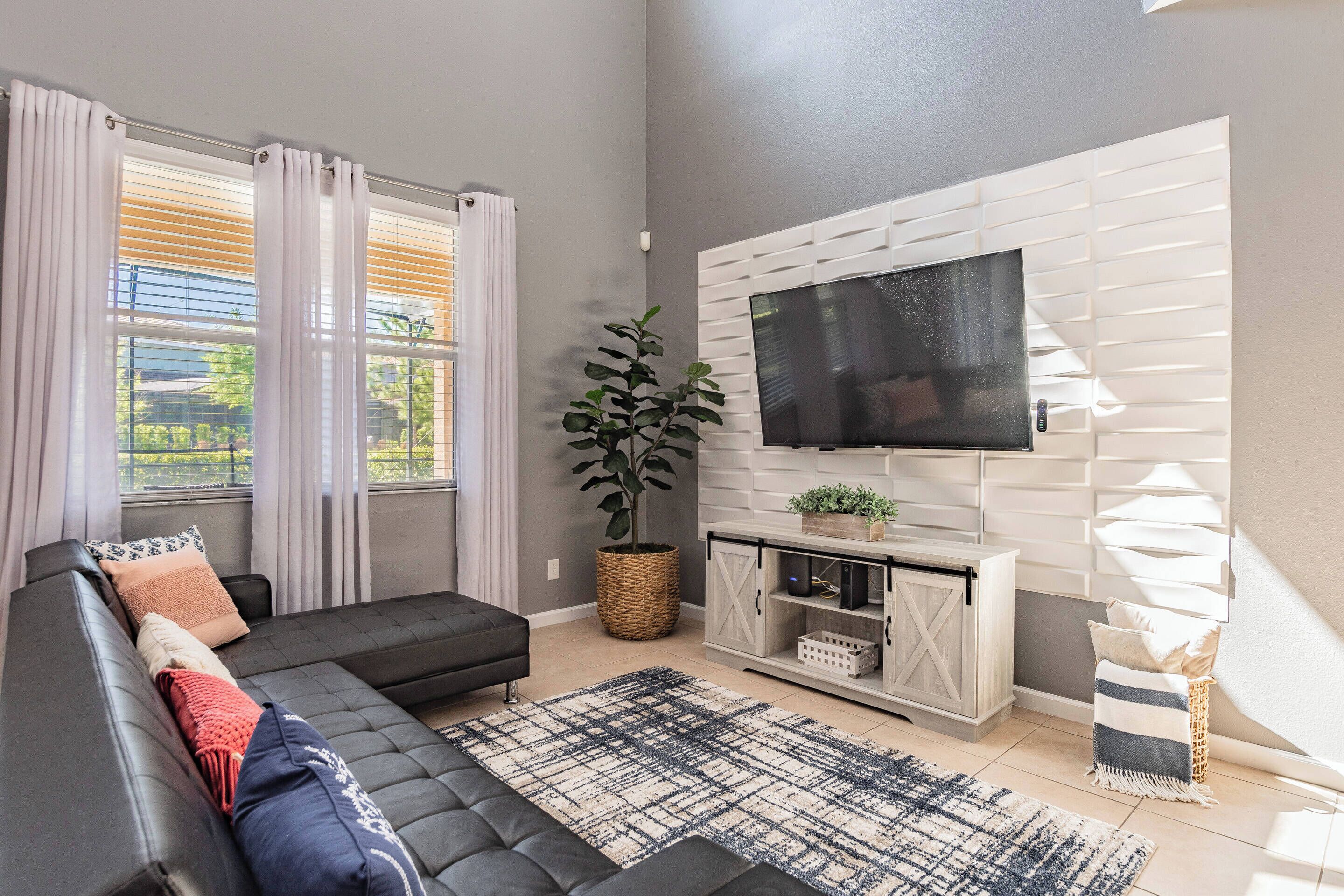 A modern living room with a sectional sofa, a flat-screen TV mounted on a white wall, a potted plant, and a wicker basket.