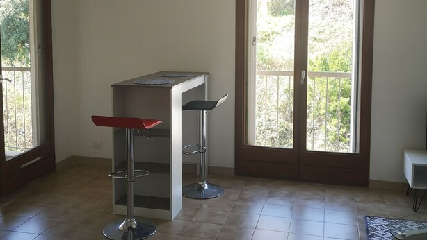 Una habitación con mostrador de cocina, dos taburetes altos, una lámpara de techo y grandes puertas correderas de vidrio que dan a un balcón.