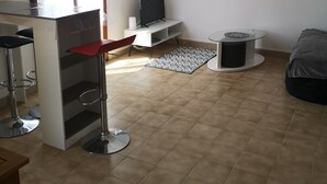 Una sala de estar moderna con televisor, una mesita redonda pequeña, un sofá y una zona de bar con taburetes.