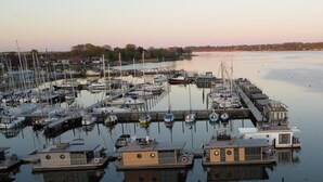 Una marina con diverse imbarcazioni ormeggiate, una banchina che si protende nell'acqua e un lago tranquillo con una costa lontana.