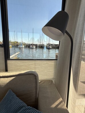 A view from a window of a boat with a sofa and a lamp, overlooking a marina with several boats.