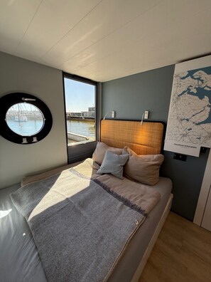 A modern bedroom with a bed, a round window, a map on the wall, and a view of a marina.