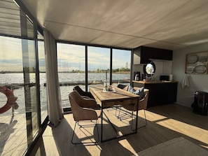 A modern interior with a dining area, kitchen, and large windows overlooking a body of water.