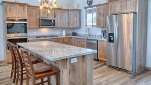 A kitchen with wooden cabinets, stainless steel appliances, a granite countertop, and a hanging light fixture. - Gorgeous Lazy Bear Inn (Show Low)
