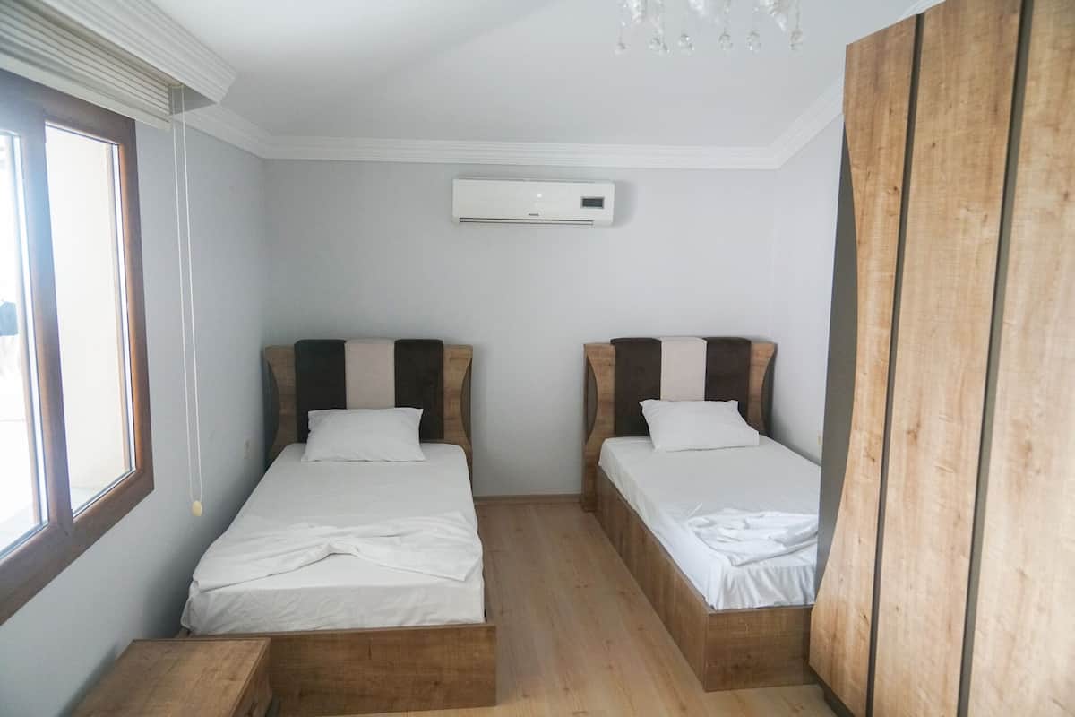 A bedroom with two beds, a wooden wardrobe, and an air conditioning unit.