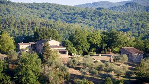 A stone building with a tiled roof surrounded by trees and hills.