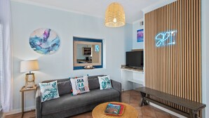 Una sala de estar moderna con un sofá gris, una mesa de centro redonda de madera, un televisor y un letrero de neón en la pared.