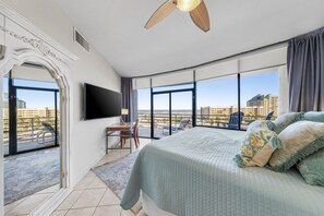 A spacious bedroom with a large bed, a flat-screen TV, and a balcony with a city view.