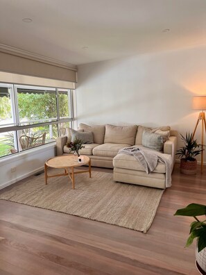 Relax in this serene living space with a view of lush greenery, featuring a comfortable sofa, coffee table, and potted plant.