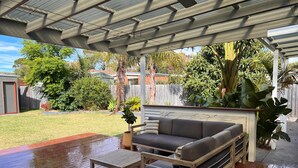 A covered outdoor patio with a wooden bench, a cushioned sofa, and a small table. - Leisure escape (Rosebud)