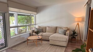 A living room with a beige sectional sofa, a round wooden coffee table, a floor lamp, and a potted plant. - Leisure escape (Rosebud)