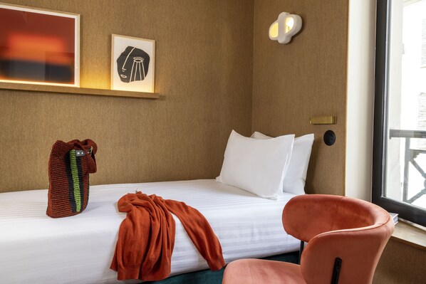 Una habitación de hotel con una cama, una silla, una lámpara de pared y un cuadro enmarcado.