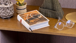 A wooden table with a book, glasses, a lamp, a beanie, and a small plant. - Hotel Ernest (Paris)