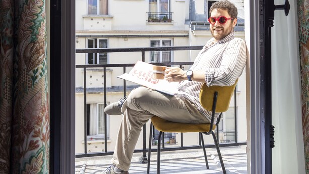 A man sitting on a yellow chair by a window with a view of buildings. - Hotel Ernest (Paris)