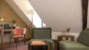 A modern room with a green sofa, a wooden table, a desk with a computer, a lamp, and a small plant. - Hotel Ernest (Paris)