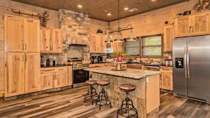 Eine moderne Küche mit Holzschränken, einer großen Kochinsel mit Barhocker, Edelstahlgeräten und einer Wand mit Natursteinverkleidung.
