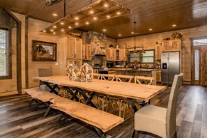 A rustic kitchen with wooden cabinets, a large wooden table, and a stone fireplace. - Huckleberry Hill: Indoor Pool, Game & Theater Room! Hot Tub, Luxury, near Attractions! (Sevierville)