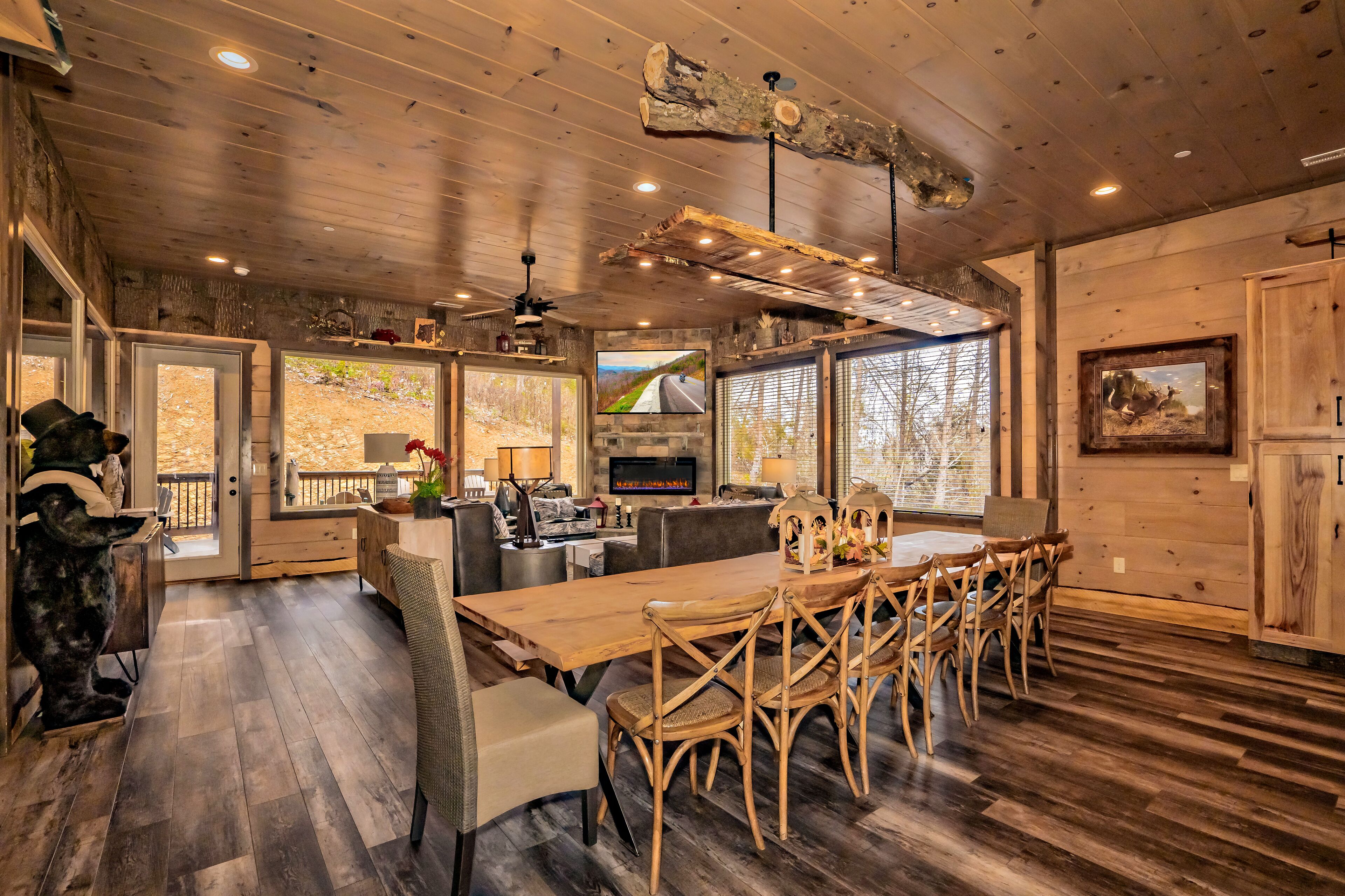 A spacious living room with a wooden ceiling, large windows, a fireplace, and a television.