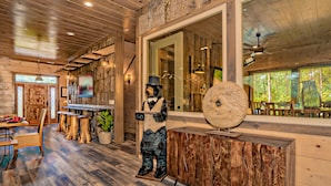 Ein rustikales Holzinterieur mit einer Bärenstatue, Holzdielen und einem großen Spiegel, der einen Blick auf einen Wald reflektiert.