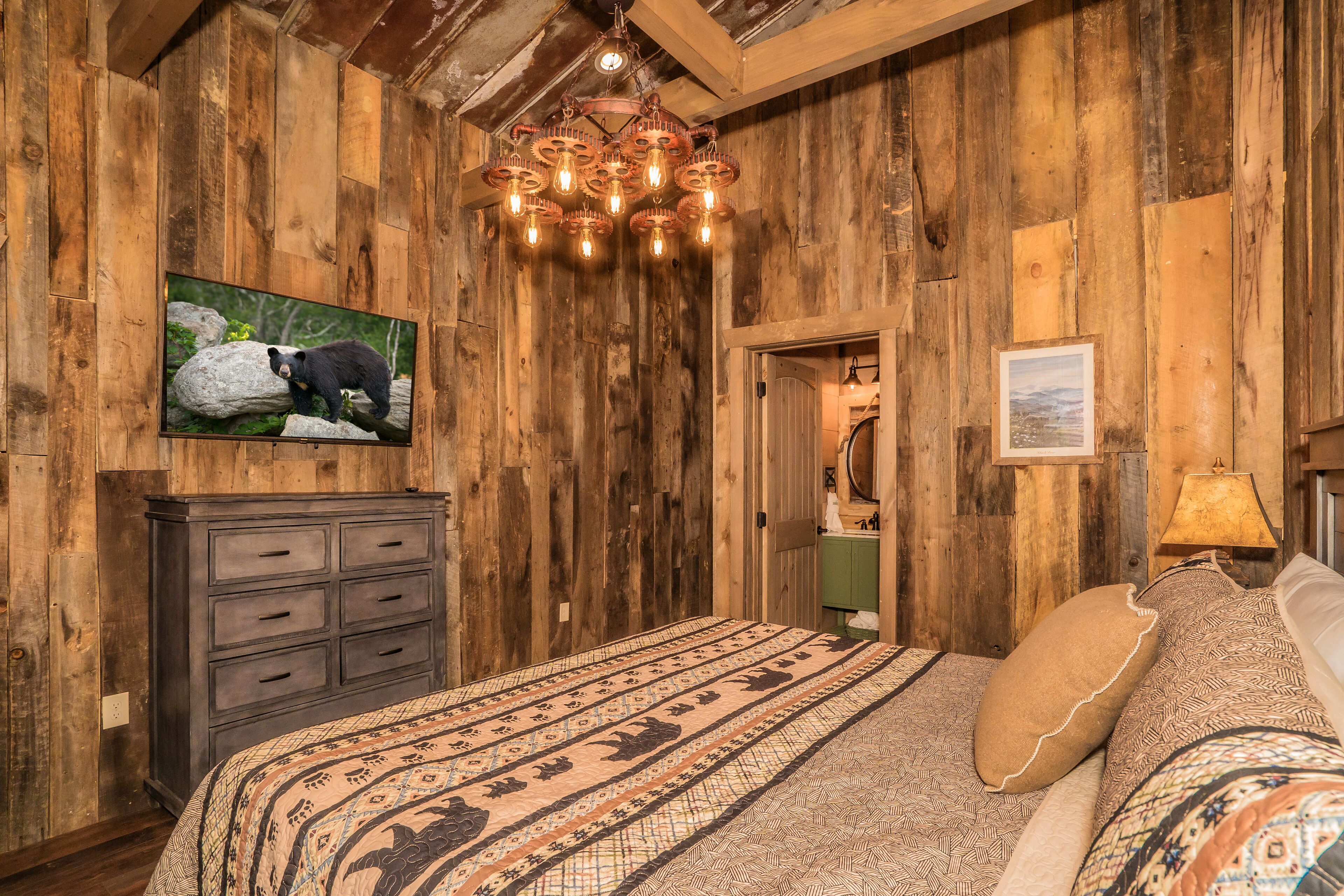 A rustic wooden room with a bed, a dresser, a chandelier, and a painting of a bear on the wall.