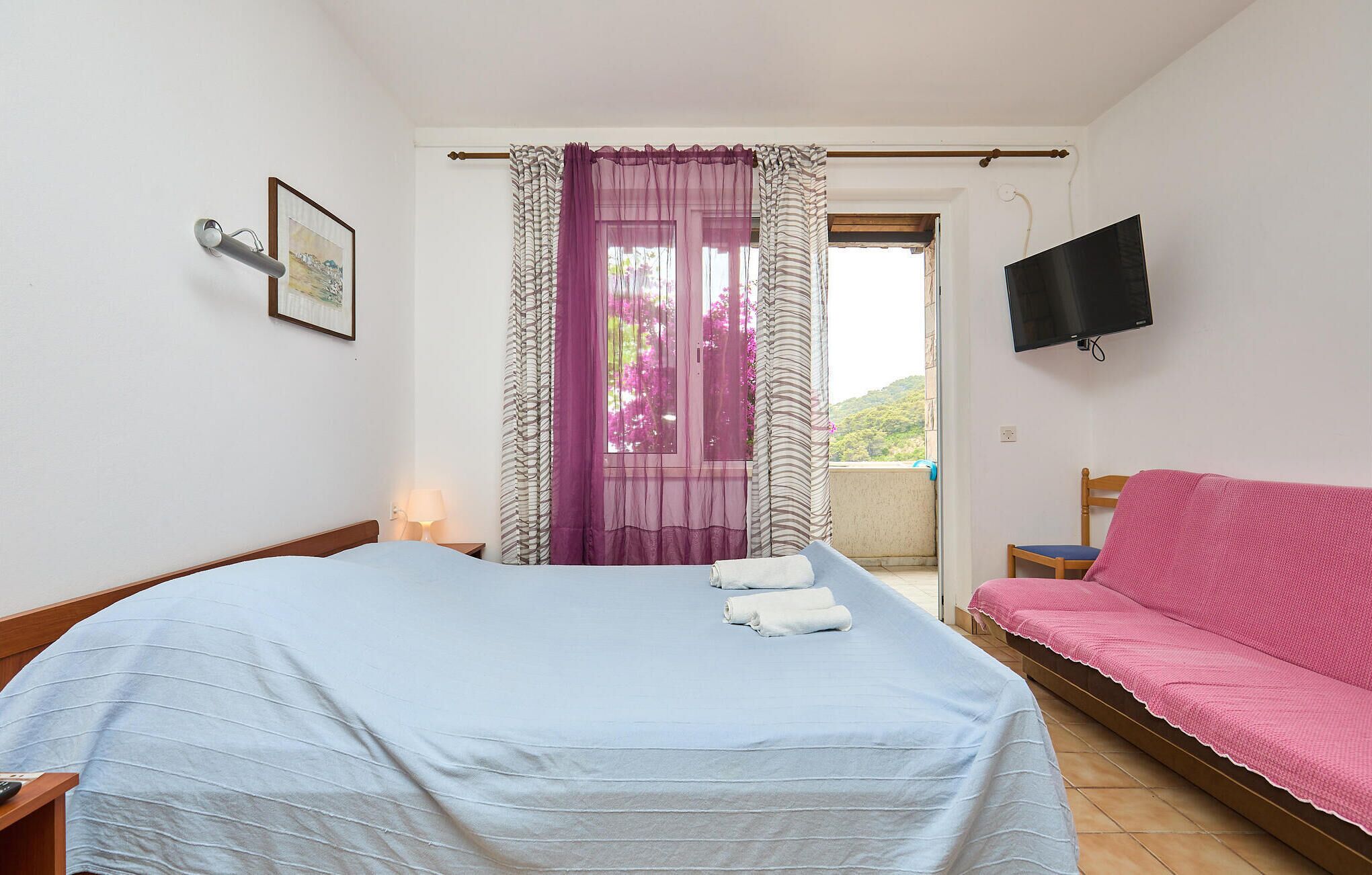Una camera da letto con un letto, un divano rosa, una TV e una finestra con tende.
