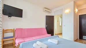Een kamer met een bed, een stoel, een televisie, een airconditioning en een deur naar een andere kamer.