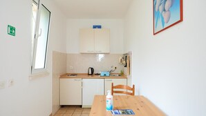 Een kleine kitchenette met een spoelbak, waterkoker en een tafel met stoel. Een raam met uitzicht op de omgeving.