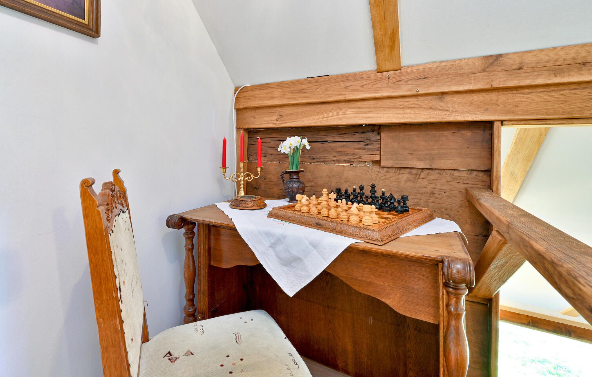 A wooden desk with a chessboard, a vase with flowers, and two red candles.