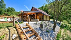 Un chalet rustique en bois, doté d’un porche couvert, d’un jacuzzi et d’un chemin de gravier menant à l’entrée.