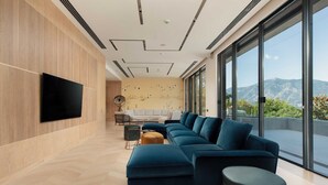 Un salon moderne doté d’un grand canapé d’angle, d’un téléviseur à écran plat fixé au mur et d’une grande fenêtre offrant une vue sur les montagnes.