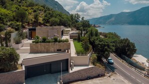 Une maison moderne avec un garage, une allée et une vue sur un lac où l’on peut voir des bateaux.