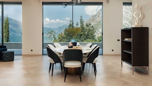 Un espace repas moderne offrant une vue panoramique sur les montagnes, avec une table ronde et des chaises, ainsi qu’une bibliothèque en bois foncé.