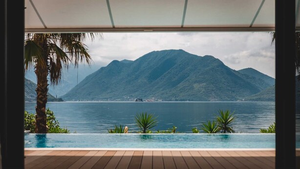 Vista da un'area a bordo piscina con un pontile di legno, una palma e una catena montuosa sullo sfondo.