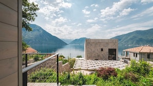Un edificio moderno con facciata in pietra affacciato su un lago, immerso nel verde e circondato da montagne.