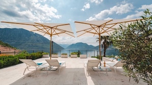 Una terrazza con posti a sedere all'aperto e ombrelloni, vista su un lago con montagne sullo sfondo.