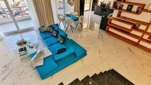 Un salon moderne avec un canapé d’angle bleu, une table basse en verre et un coin repas avec une nappe bleue.