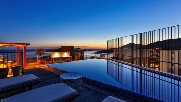 Un espace piscine aménagé sur le toit, doté d’une balustrade en verre, de chaises longues et d’un barbecue.