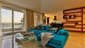 Un salon moderne avec un canapé turquoise, une table basse en verre et une bibliothèque rouge.
