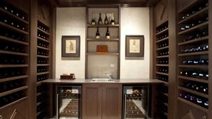 A wine cellar with wooden shelving, a central counter, and two framed pictures. - Alexandar Suits & Spa 401 (Budva)