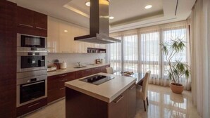 A modern kitchen with built-in appliances, a central island, and large windows. - Alexandar Suits & Spa 401 (Budva)