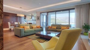 A modern living room with a sofa set, a coffee table, and a yellow armchair. There is a dining area with a table and chairs, and a kitchen in the background. - Alexandar Suits & Spa 401 (Budva)