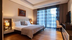 Habitació d'hotel amb un llit gran, una taula de treball amb una cadira, una televisió i una finestra amb cortines.