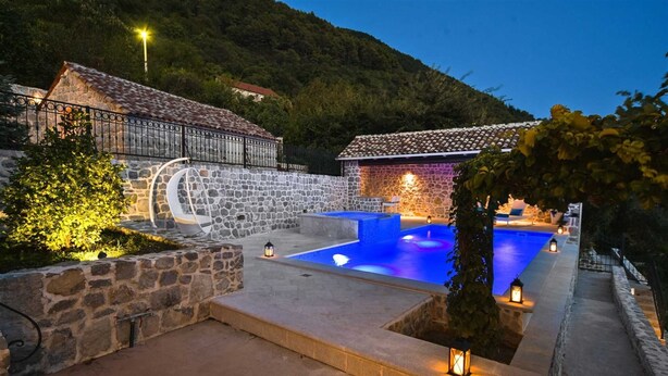 A stone-walled pool area with a clear blue pool, surrounded by stone steps and walls, and a small seating area with a lantern. - Classic  Estate  Villa (Kotor)