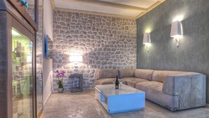 Een moderne woonkamer met een stenen muur, een blauwe salontafel, een beige bank en een glazen kast met wijnflessen.